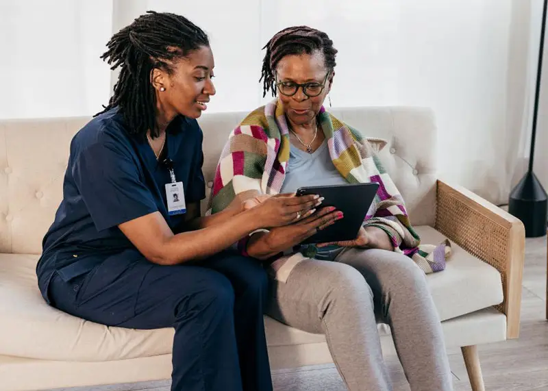 Two women on couch review medical records on a tablet